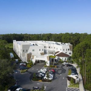 Aerial view of a large building surrounded by trees with a parking lot in the foreground.