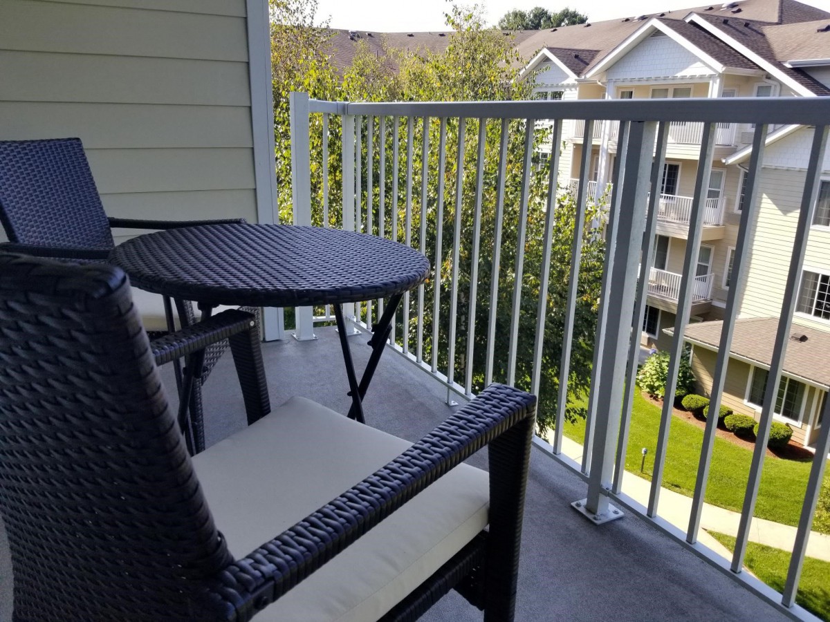 A cozy balcony with a wicker table and chair set overlooking a suburban apartment complex.