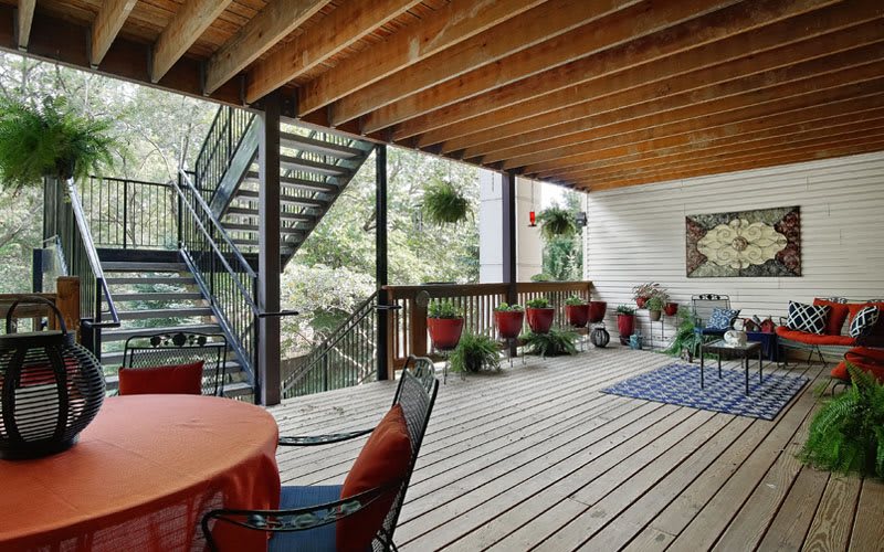 A cozy outdoor patio with wooden flooring, decorated with plants and comfortable furniture.