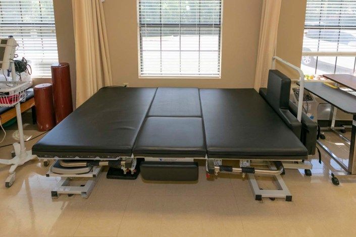 An adjustable massage table with black cushioning, positioned indoors near a window.