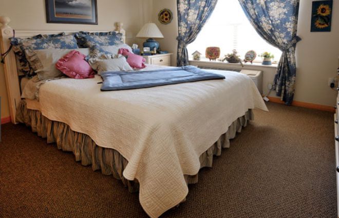 A cozy bedroom with a neatly made bed adorned with pillows and a large window with floral curtains.