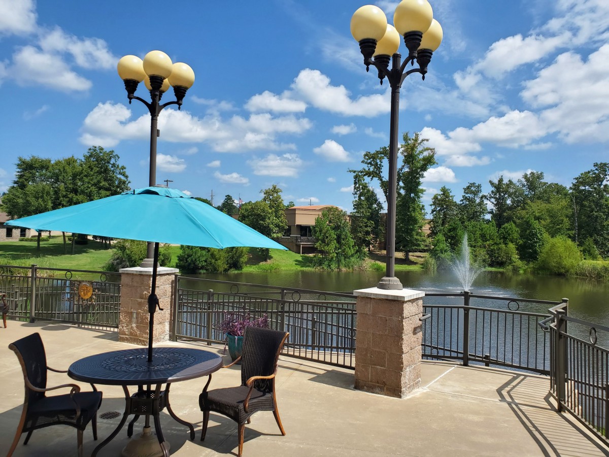 A scenic outdoor patio overlooking a lake with fountains and surrounded by greenery.