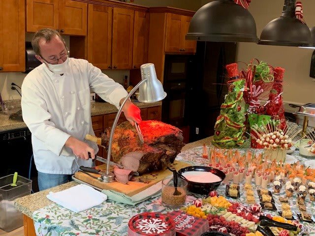 A chef carves a roast at a holiday buffet, surrounded by various festive dishes and decorations.
