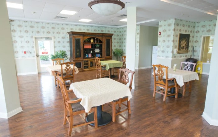 A bright dining room with wooden tables and chairs, featuring a decorated bookshelf and natural lighting.