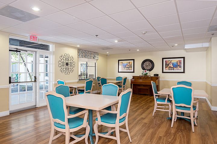 A bright and welcoming dining area featuring tables and chairs, decorated with wall art and a wooden floor.