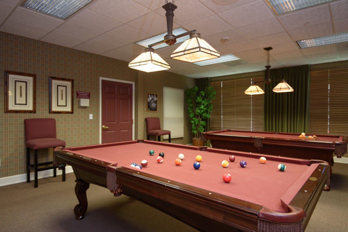 A game room featuring a pool table with balls arranged, under warm lighting.