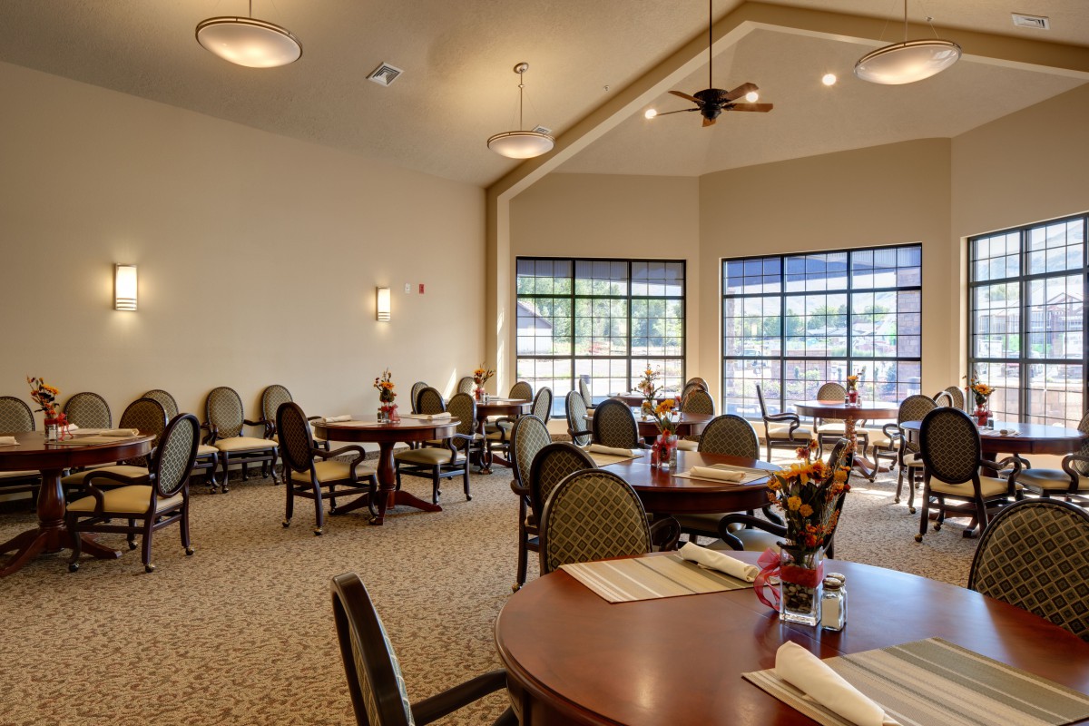 A spacious dining area with neatly arranged tables and chairs, illuminated by ceiling lights and natural daylight through large windows.