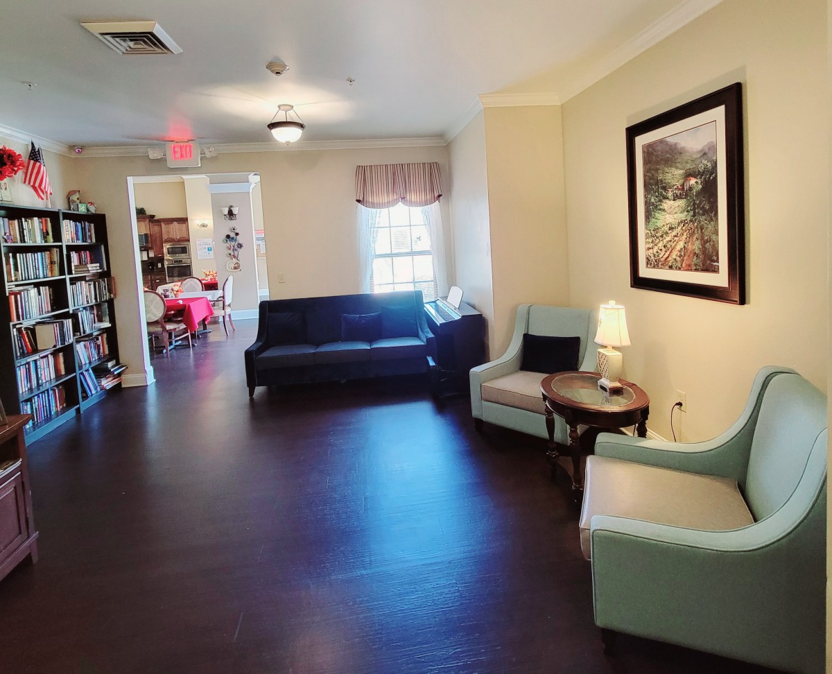 A cozy living room with sofas, chairs, a small table with a lamp, and a painting on the wall.