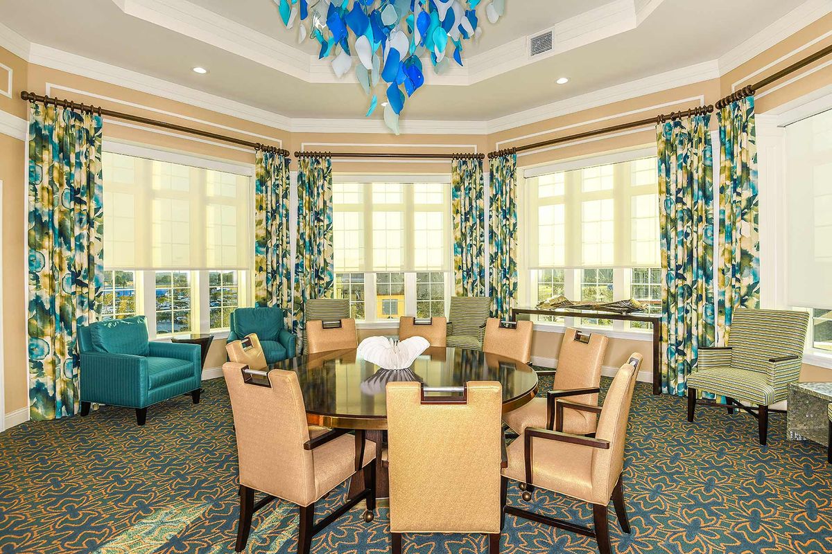 A modern dining room with stylish furniture, a chandelier, and large windows adorned with decorative curtains.