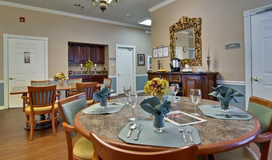 A well-decorated dining room with a round table set for a meal, featuring floral centerpieces and elegant place settings.