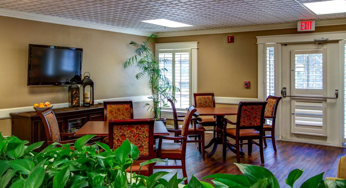 A cozy dining area with wooden tables and chairs, featuring large windows allowing natural light to illuminate the space.