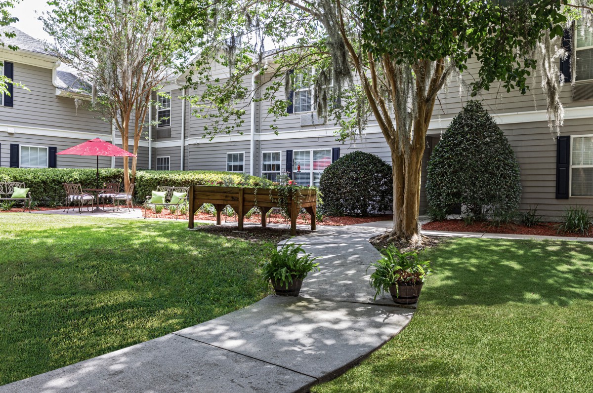 A serene garden with a winding pathway surrounded by lush greenery and residential buildings.