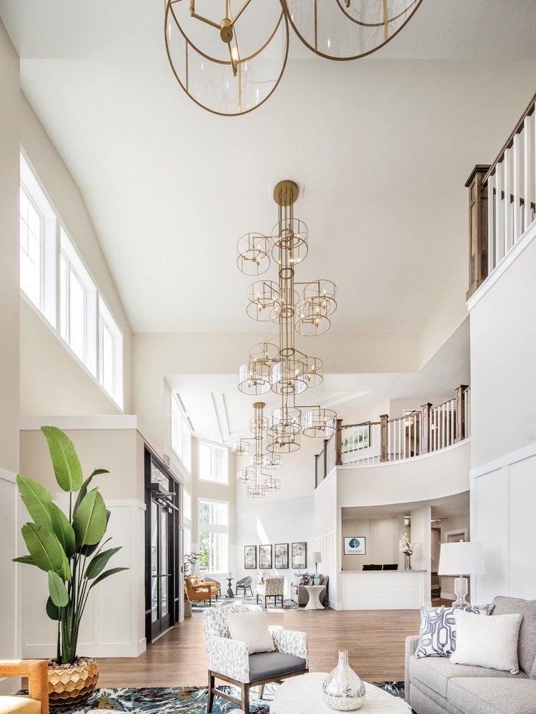 Spacious modern living room with high ceilings and a striking chandelier, featuring a balcony and decorative plants.