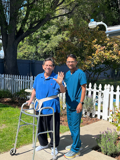 A caregiver assists an elderly individual outdoors, both sharing a moment of joy.