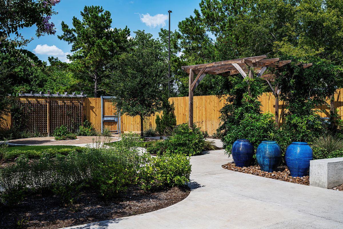 A beautifully landscaped garden with a pathway, wooden fence, and vibrant potted plants.
