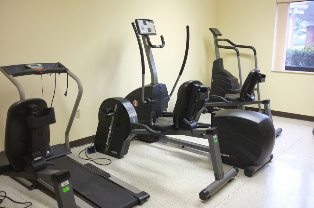 A small fitness center with various exercise machines, including a treadmill and elliptical trainers.