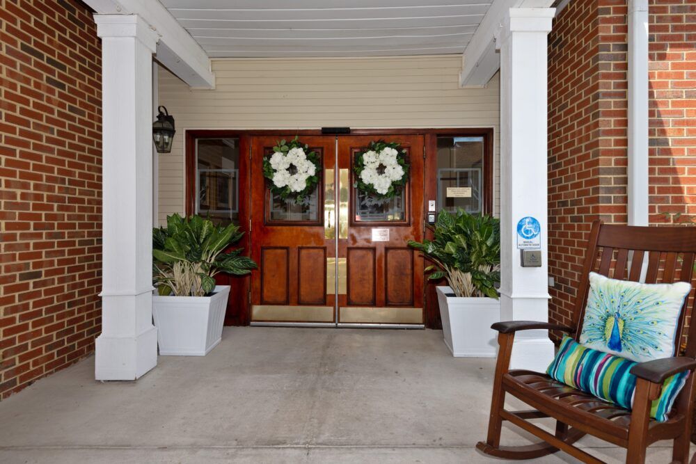 A welcoming entrance with double wooden doors adorned with wreaths, flanked by large planters and a rocking chair.