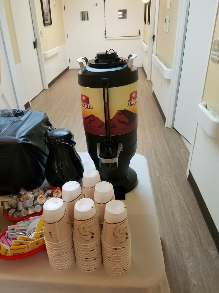 Coffee setup in a hallway with disposable cups and condiments.