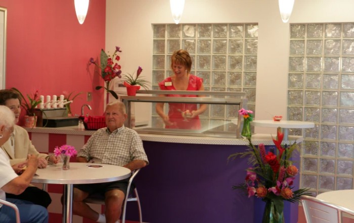 A cozy ice cream shop interior with a customer seated at a table and an employee behind the counter.