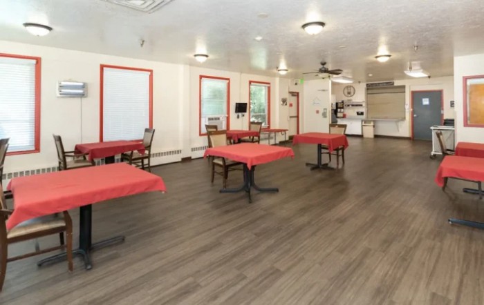 A spacious dining area with tables covered in red tablecloths and wood flooring.
