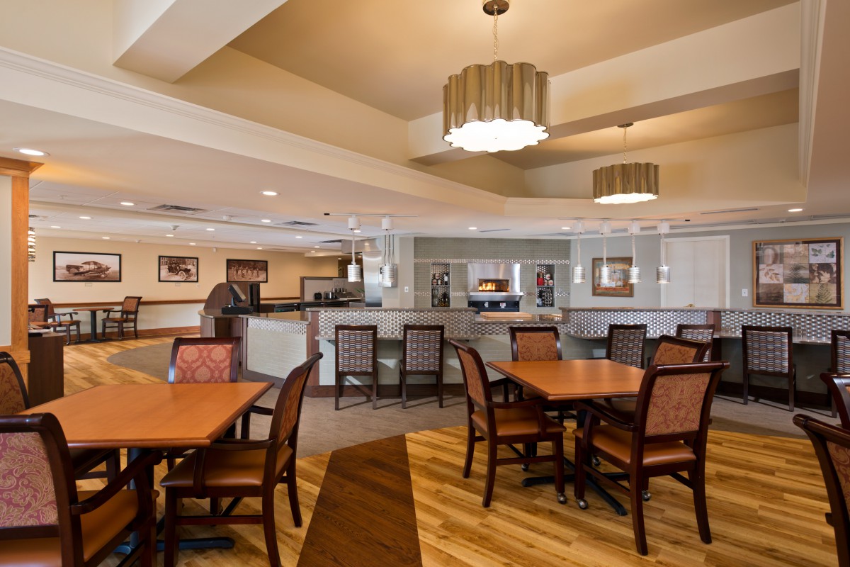 A cozy dining area with wooden flooring, tables, and chairs, illuminated by stylish lighting fixtures.