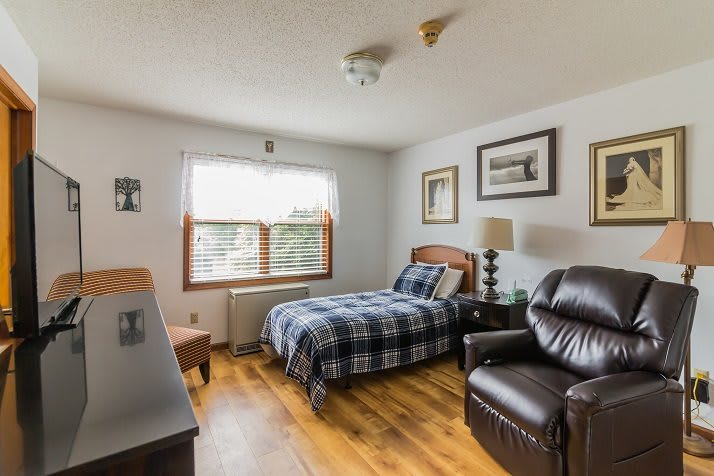 A cozy bedroom with a single bed, a leather chair, and wooden floors.