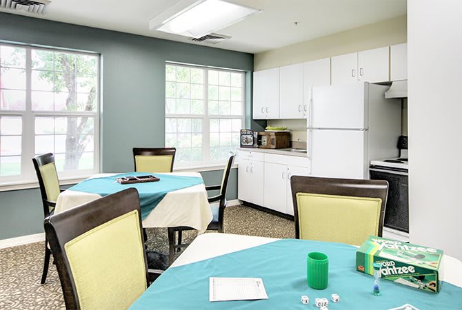 A bright kitchen and dining area with tables and chairs, featuring a microwave and ample natural light.