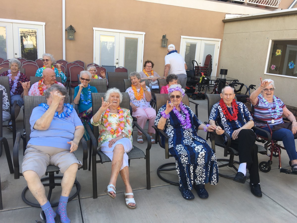 A group of elderly individuals enjoying a Hawaiian-themed outdoor party, adorned with colorful leis and festive attire.