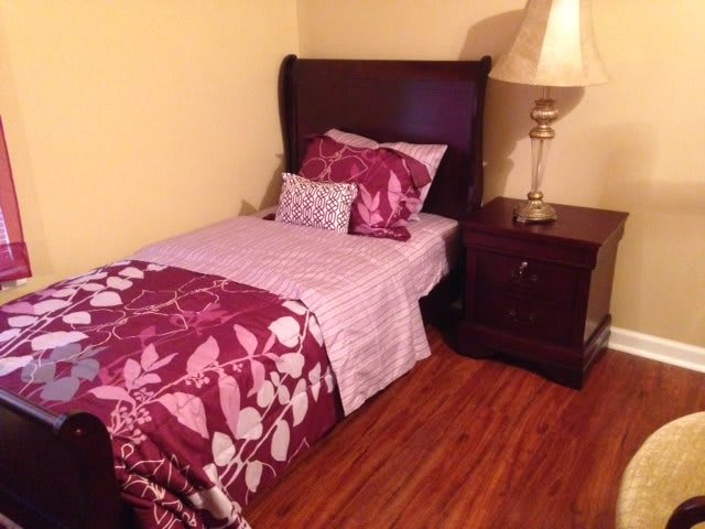 A cozy bedroom with a single bed featuring floral bedding, a nightstand, and a lamp.
