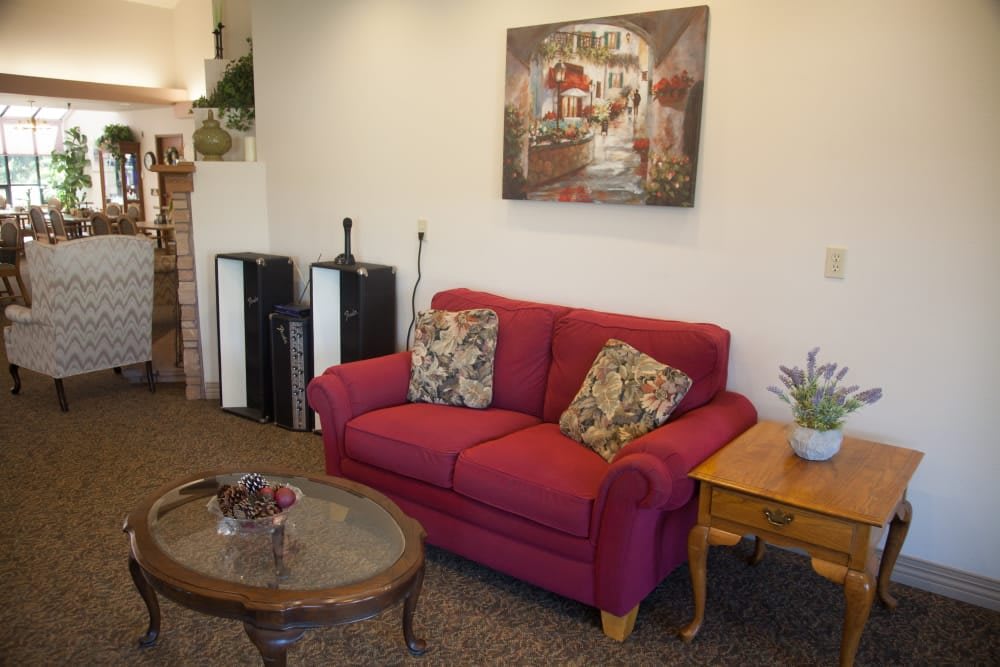 A cozy living room featuring a red sofa with floral cushions, a wooden coffee table, and a decorative painting on the wall.