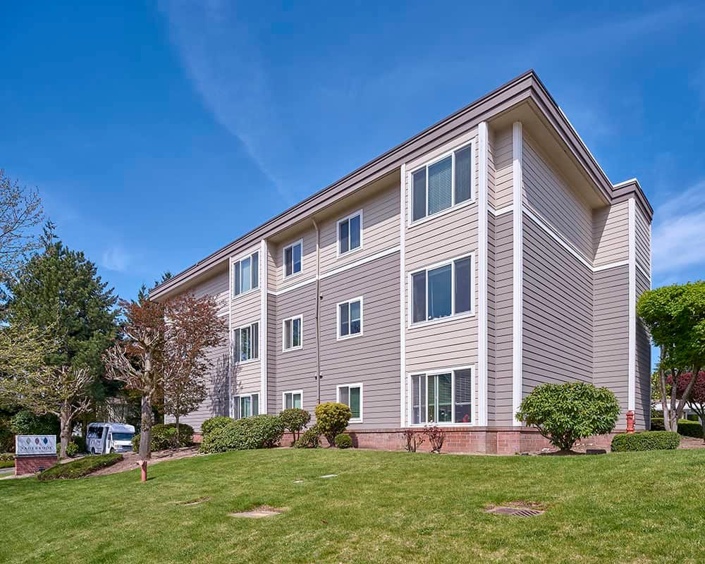 A residential apartment building with green grass and trees under a clear blue sky.