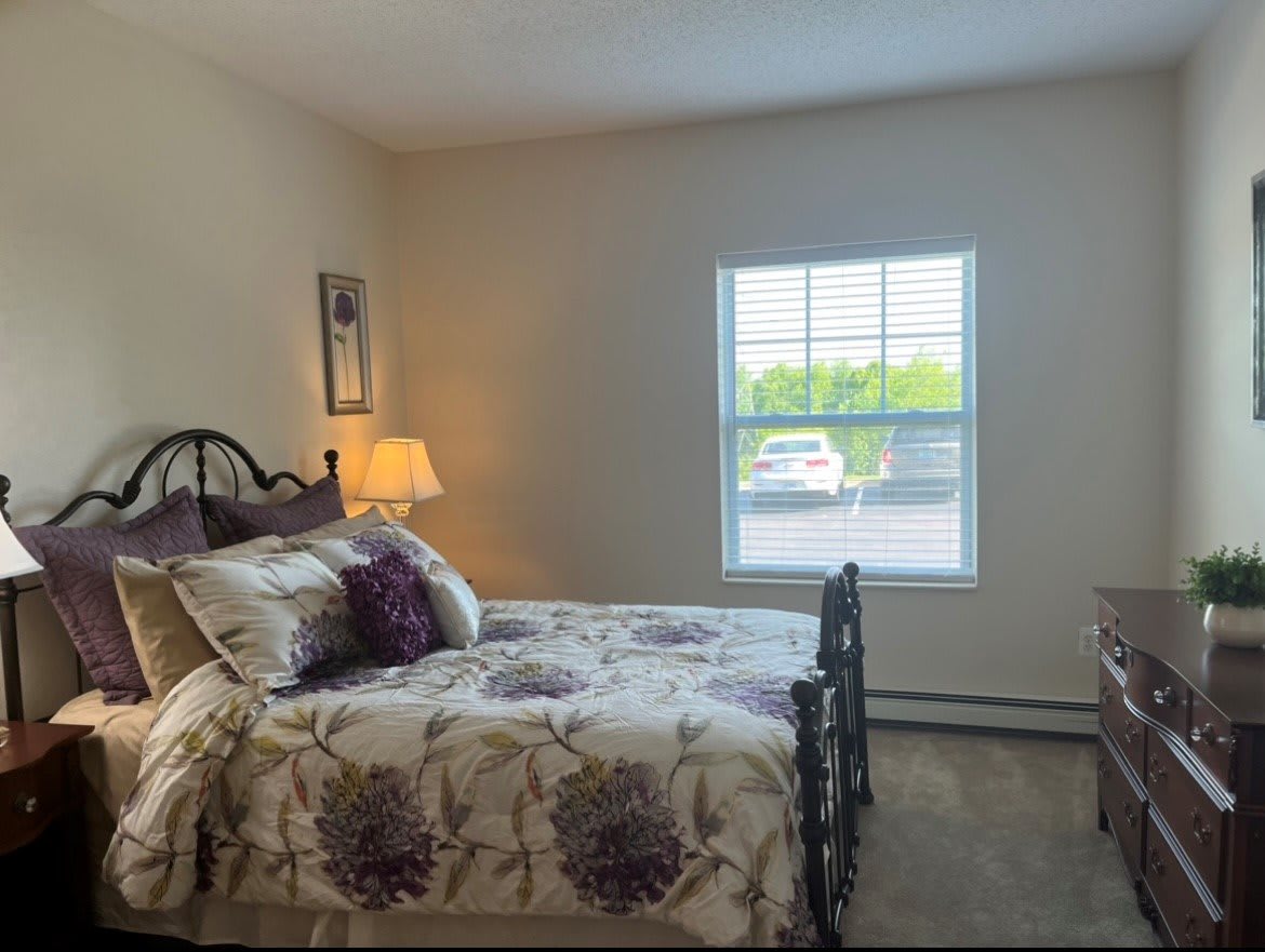 A cozy bedroom with a bed, lamp, and window view.