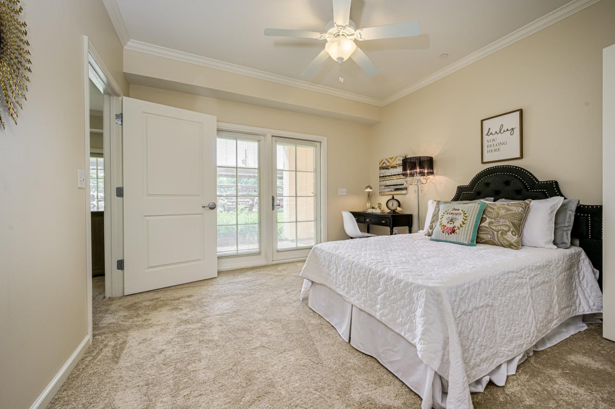 A cozy bedroom featuring a bed, desk, and ceiling fan with natural light streaming in through large glass doors.