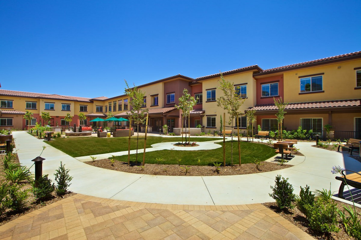 A modern building with a landscaped courtyard featuring pathways and trees under a clear blue sky.