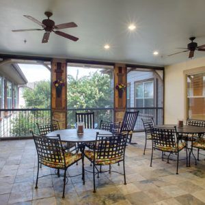 A cozy screened patio with ceiling fans, featuring several tables and chairs on a tile floor.