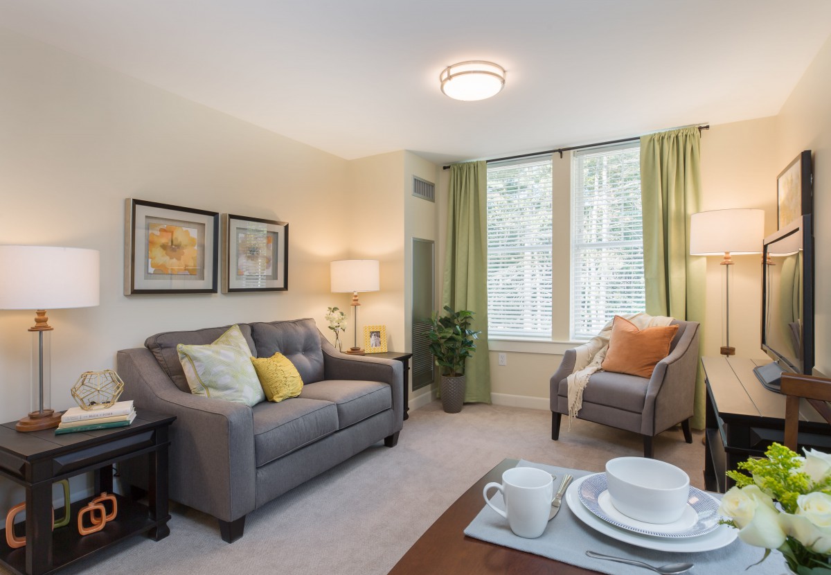 A cozy living room with a gray sofa, an armchair, and a coffee table set against large windows with green curtains.