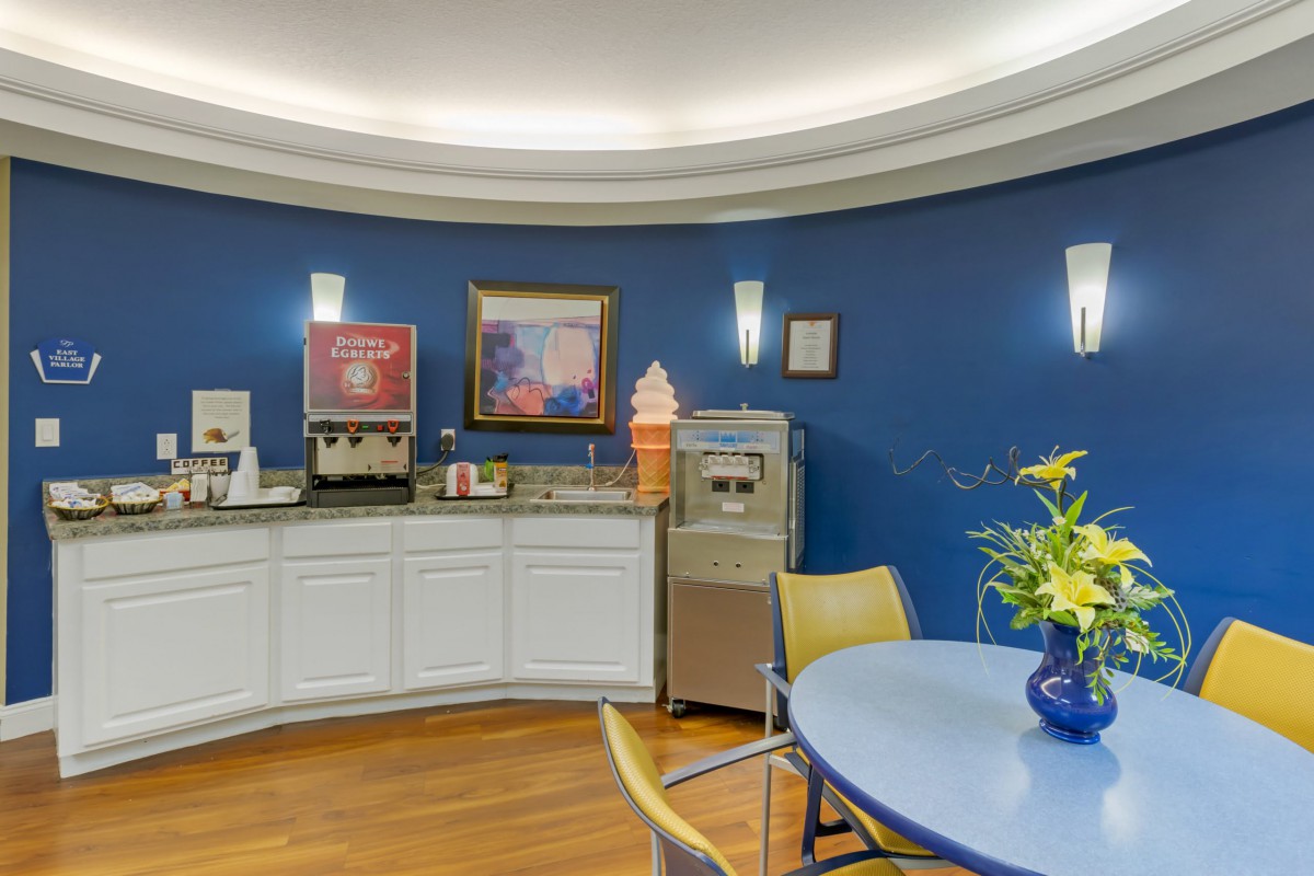 A cozy indoor space featuring a coffee station and ice cream machine against blue walls, with a round table and chairs for seating.