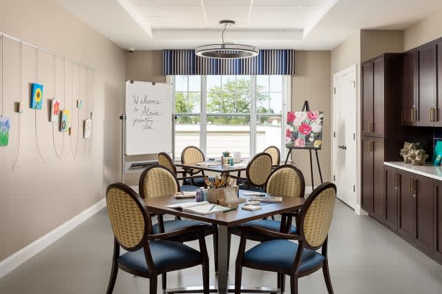 A well-lit dining area with tables and chairs, featuring art supplies and a large window.