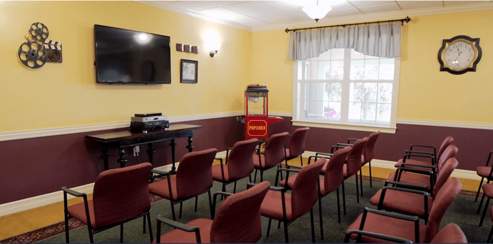 A small meeting room with rows of chairs, a television, a projector, and a popcorn machine by the window.