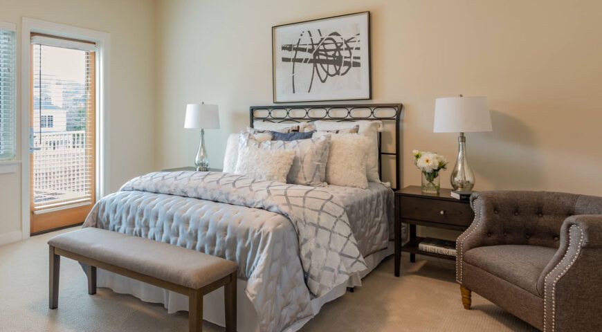A cozy and elegantly designed bedroom featuring a well-dressed bed, stylish lamps, and artistic wall decor.
