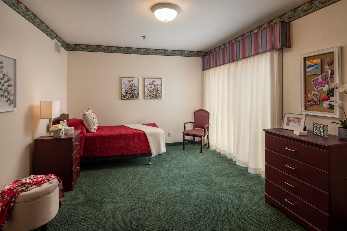A classic-style bedroom with a single bed, green carpet, and red bedding.