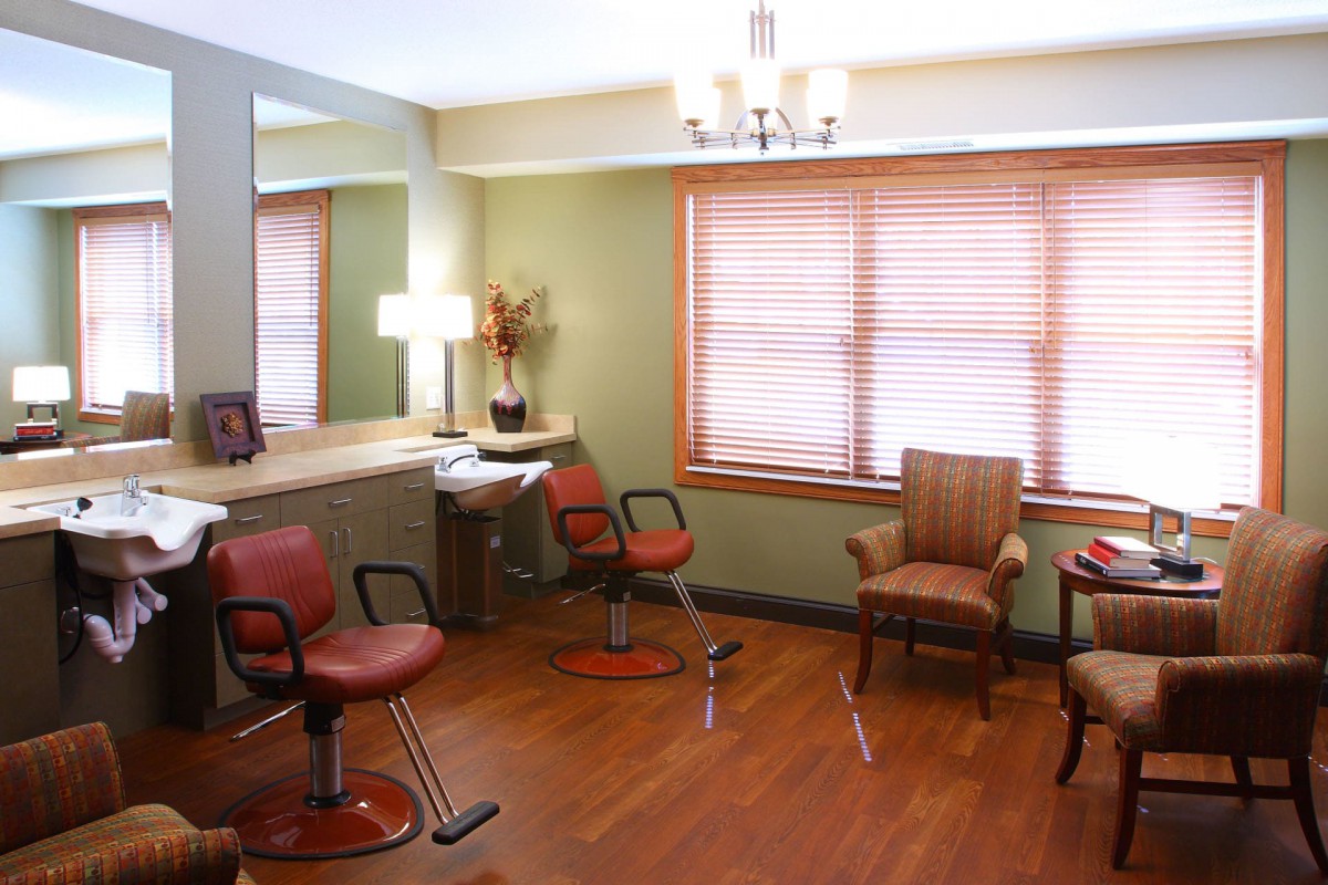 A well-lit salon with comfortable seating and large mirrors, featuring wooden flooring and elegant decor.