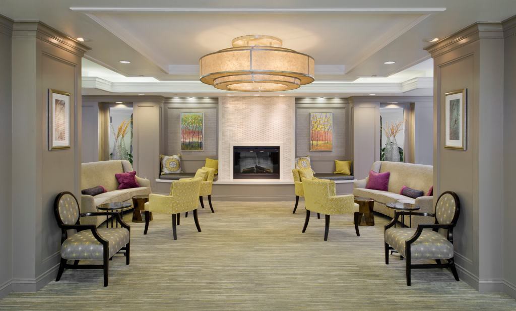 A modern lobby with a central fireplace, elegant seating, and a large chandelier.