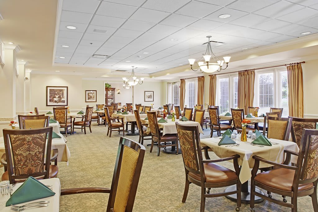 A spacious dining room with elegantly arranged tables and chairs, featuring chandeliers and a carpeted floor.