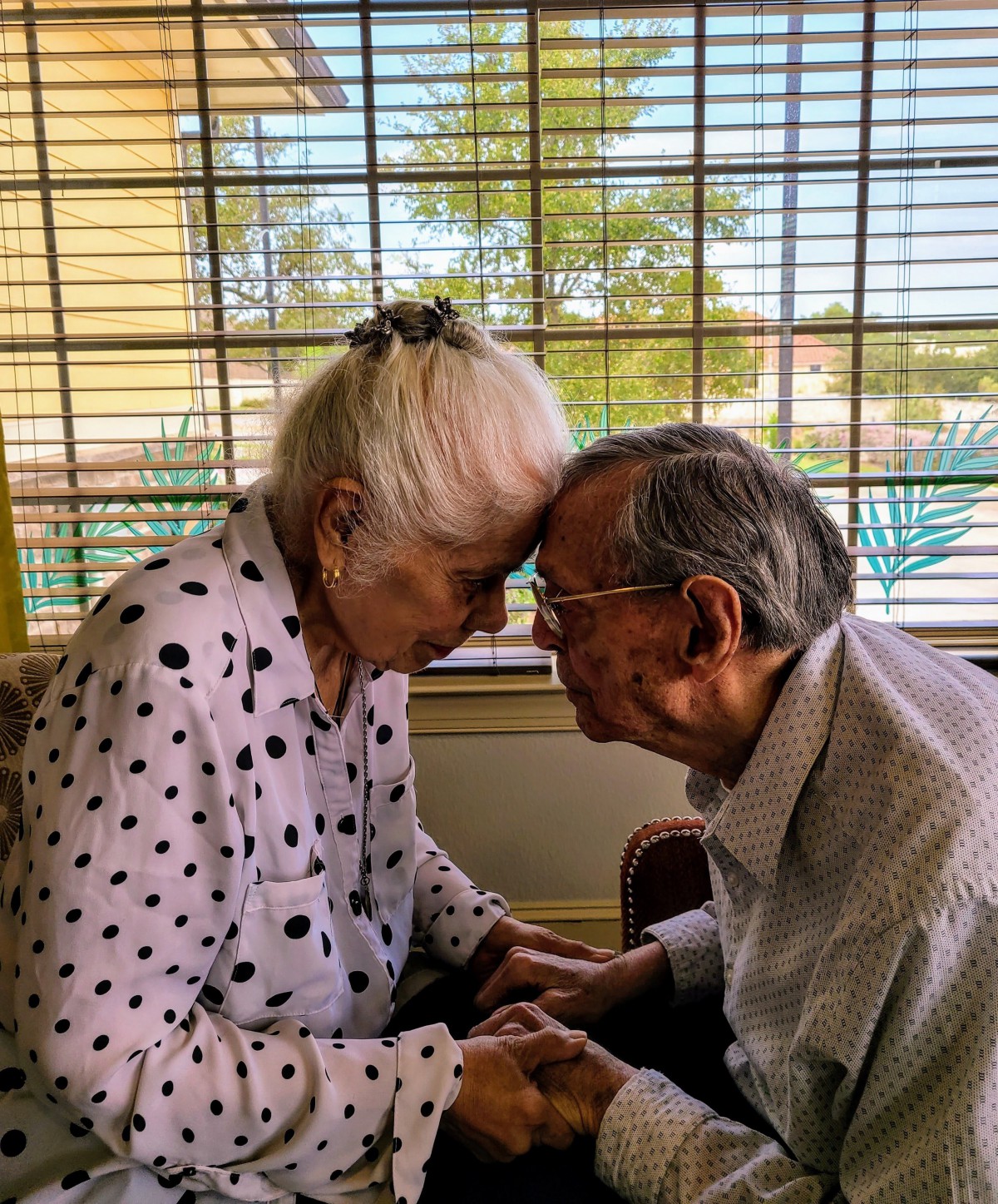 An elderly couple shares a tender moment, leaning their foreheads together in affection.