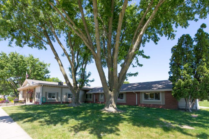 A brick house surrounded by lush trees and a well-maintained lawn.