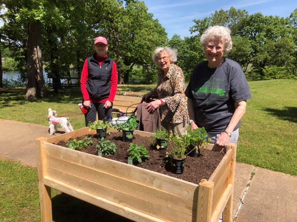 A group of people gardening together in a community space with a raised bed.
