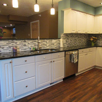 A modern kitchen with white cabinets, a patterned backsplash, and wooden flooring.