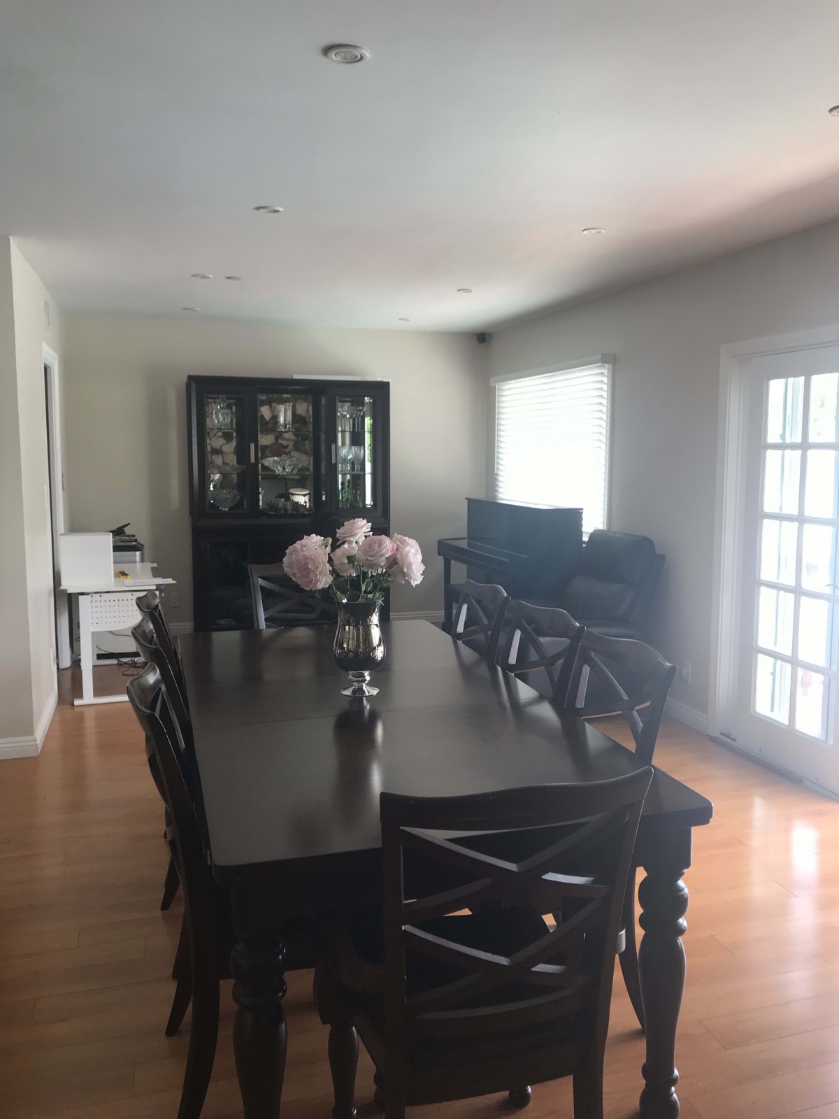 A well-lit dining room with a dark wooden table and chairs, decorated with flowers in a vase.