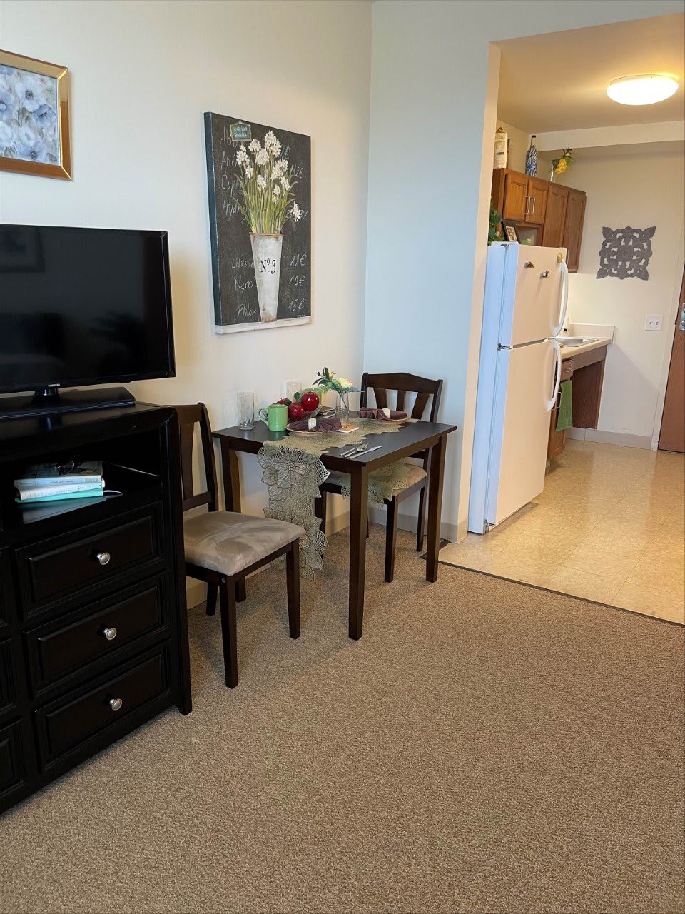 A cozy apartment setup featuring a small dining area, TV, and view into the kitchen.